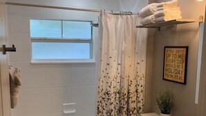 A bathroom with a bathtub, toilet, and a window. There is a shower curtain with a geometric pattern, a towel rack, and a potted plant on the vanity. - Amazing Five-Star Luxury Thornton Park two Bedroom Apt - close to Kia Center. (Orlando)