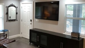 A living room with a flat-screen TV, a ceiling fan, a large mirror, and a dark wooden entertainment unit. - Amazing Five-Star Luxury Thornton Park two Bedroom Apt - close to Kia Center. (Orlando)