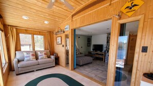 A cozy wooden cabin interior with a sofa, a television, and a dining area.