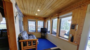 A cozy cabin interior with a wooden ceiling, a blue carpet, a sofa, and a television.
