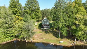 A lakeside cabin surrounded by dense forest, with a clear view of the water and a boat docked nearby.