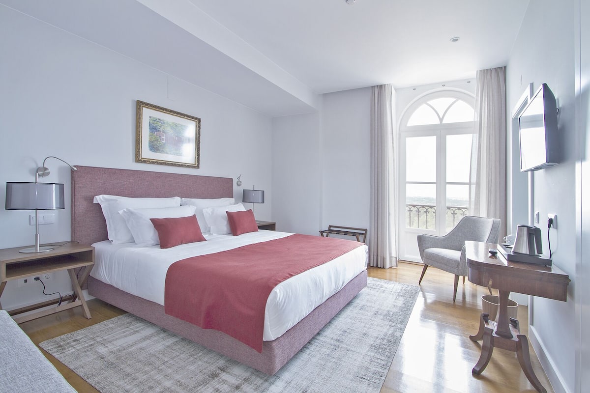 A modern hotel room with a large bed, a desk, a chair, and a TV.