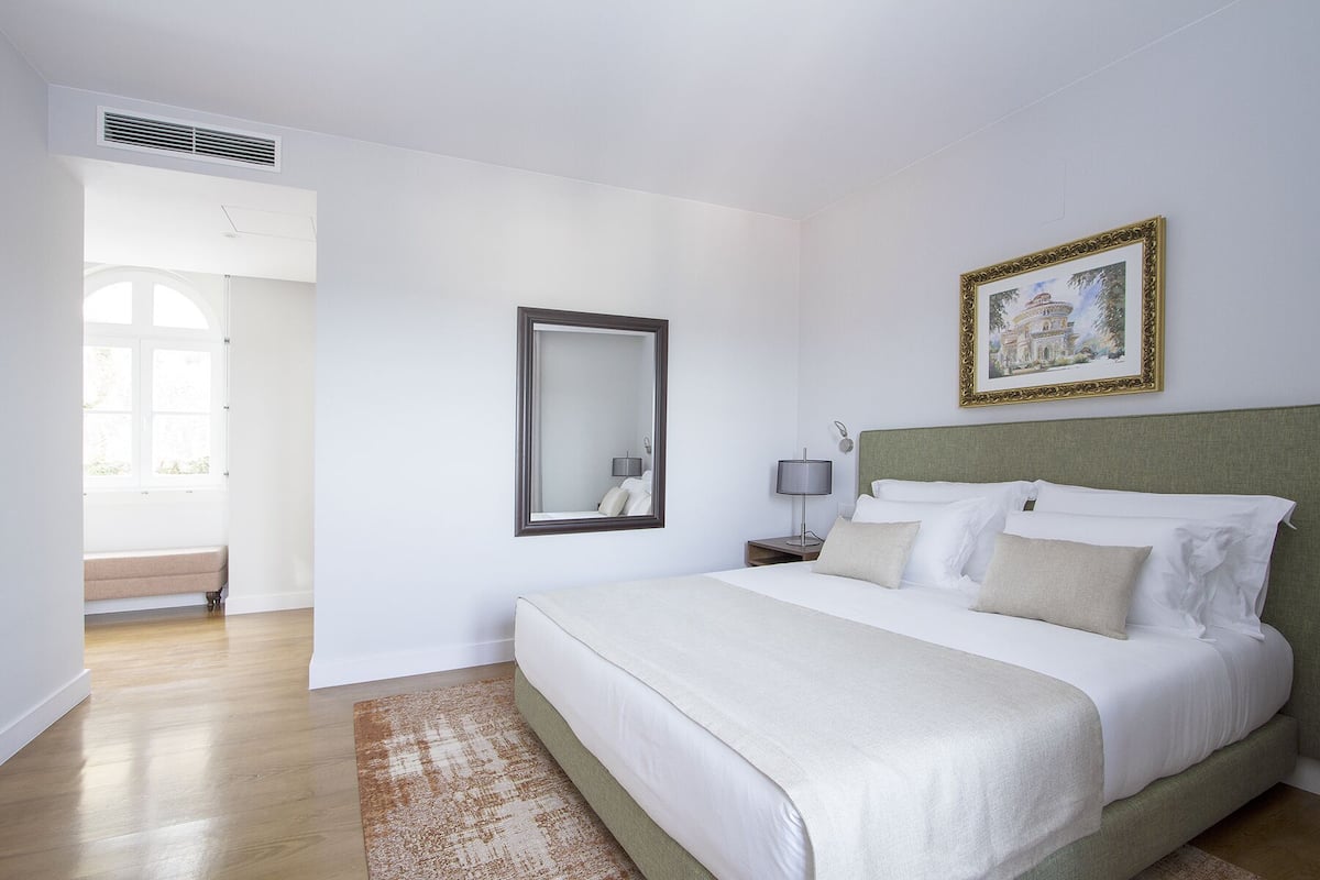 A hotel room with a large bed, a bedside table with a lamp, a mirror, and a framed picture on the wall.