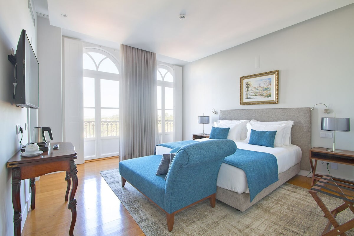 A hotel room with a large bed, a desk with a coffee maker, a TV, and a window with curtains.