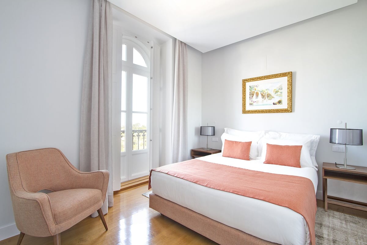 A hotel room with a large bed, two bedside tables, a chair, a window with curtains, and a framed picture on the wall.