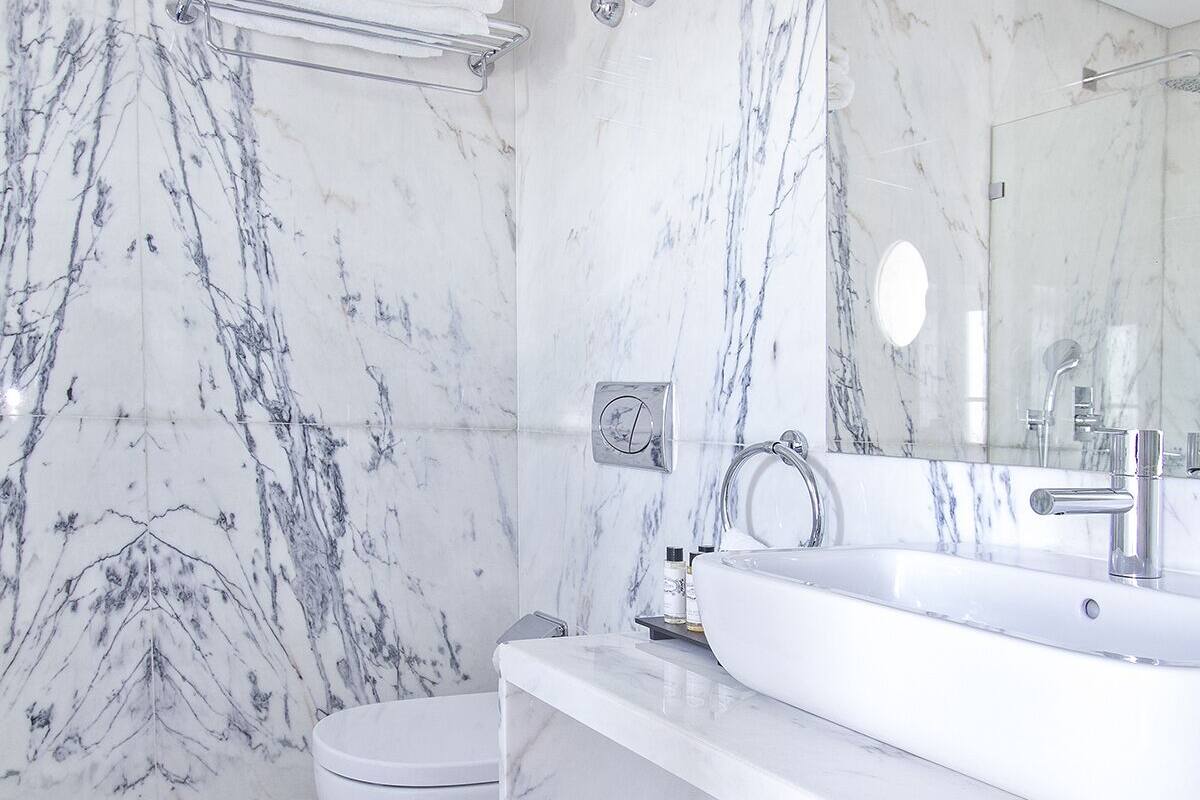 A modern bathroom with a marble floor and walls, a white sink, and a toilet.