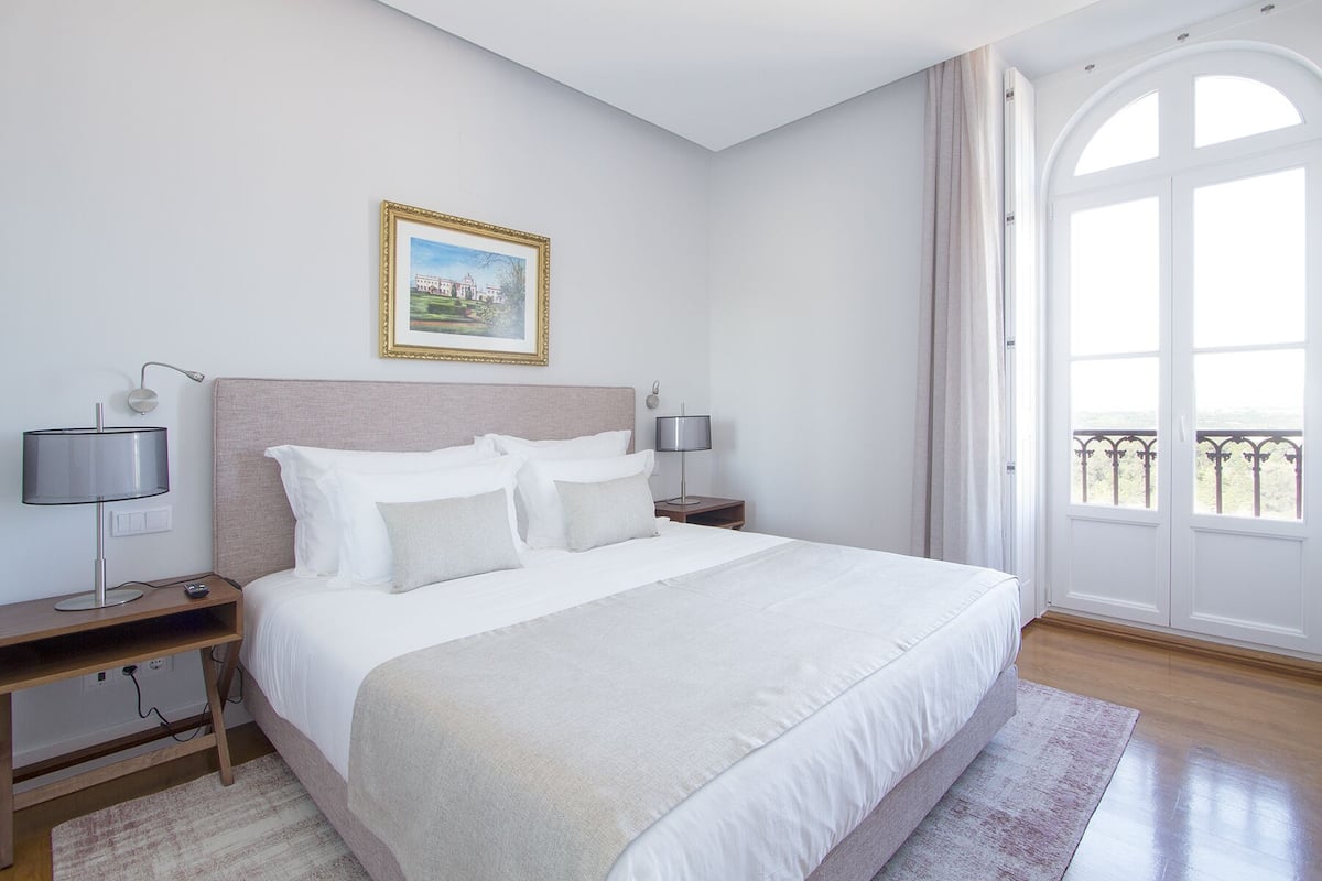 A hotel room with a large bed, two bedside tables with lamps, a framed picture on the wall, and a balcony with a view.