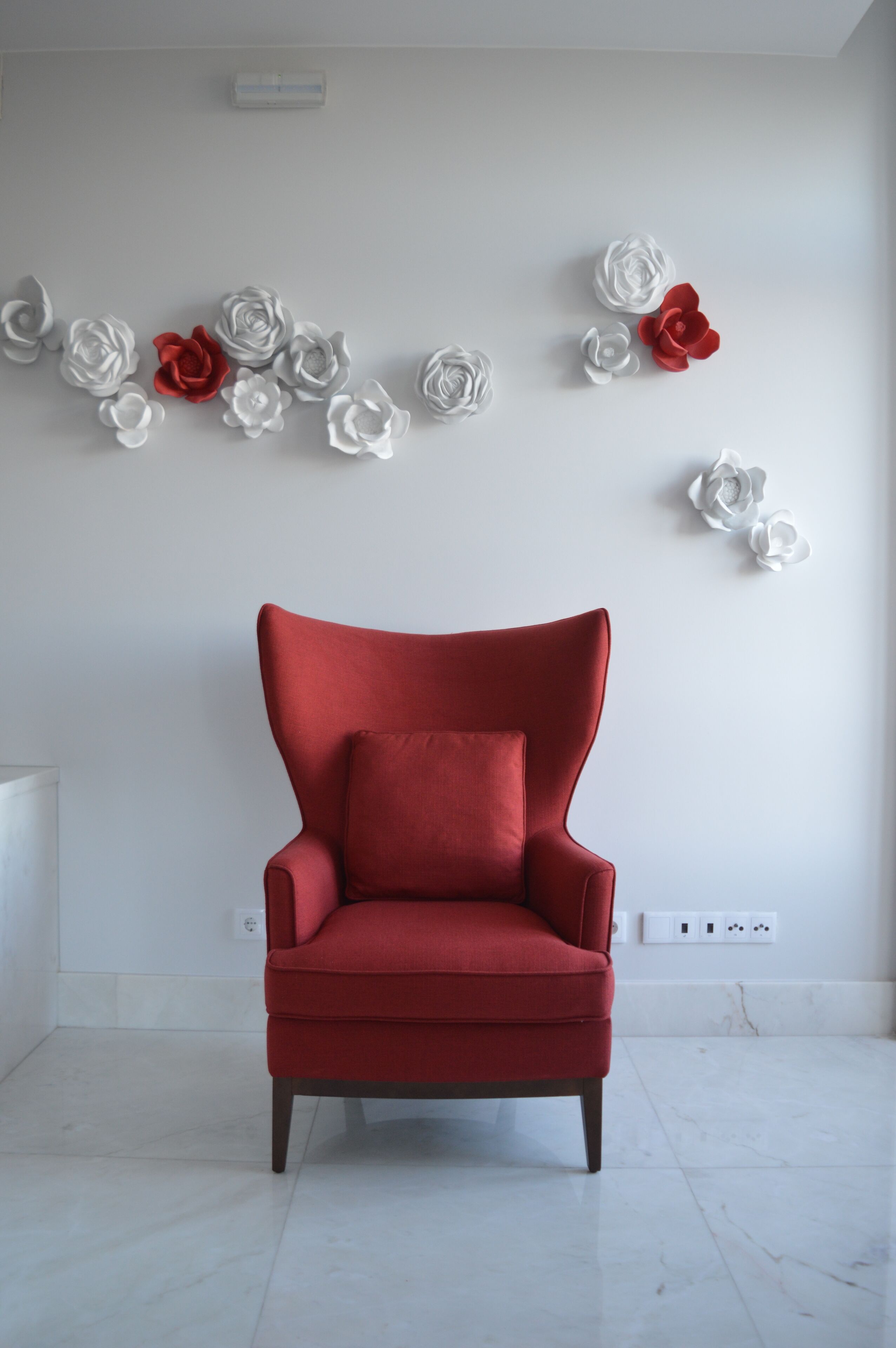A red armchair in a room with a white wall and a white floor.