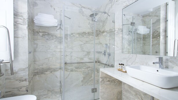 A modern bathroom with a glass-enclosed shower, marble walls, and a large mirror above a white sink. - Villa Bela Vista (Sintra)