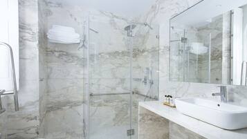 A modern bathroom with a glass-enclosed shower, marble walls, and a large mirror above a white sink.