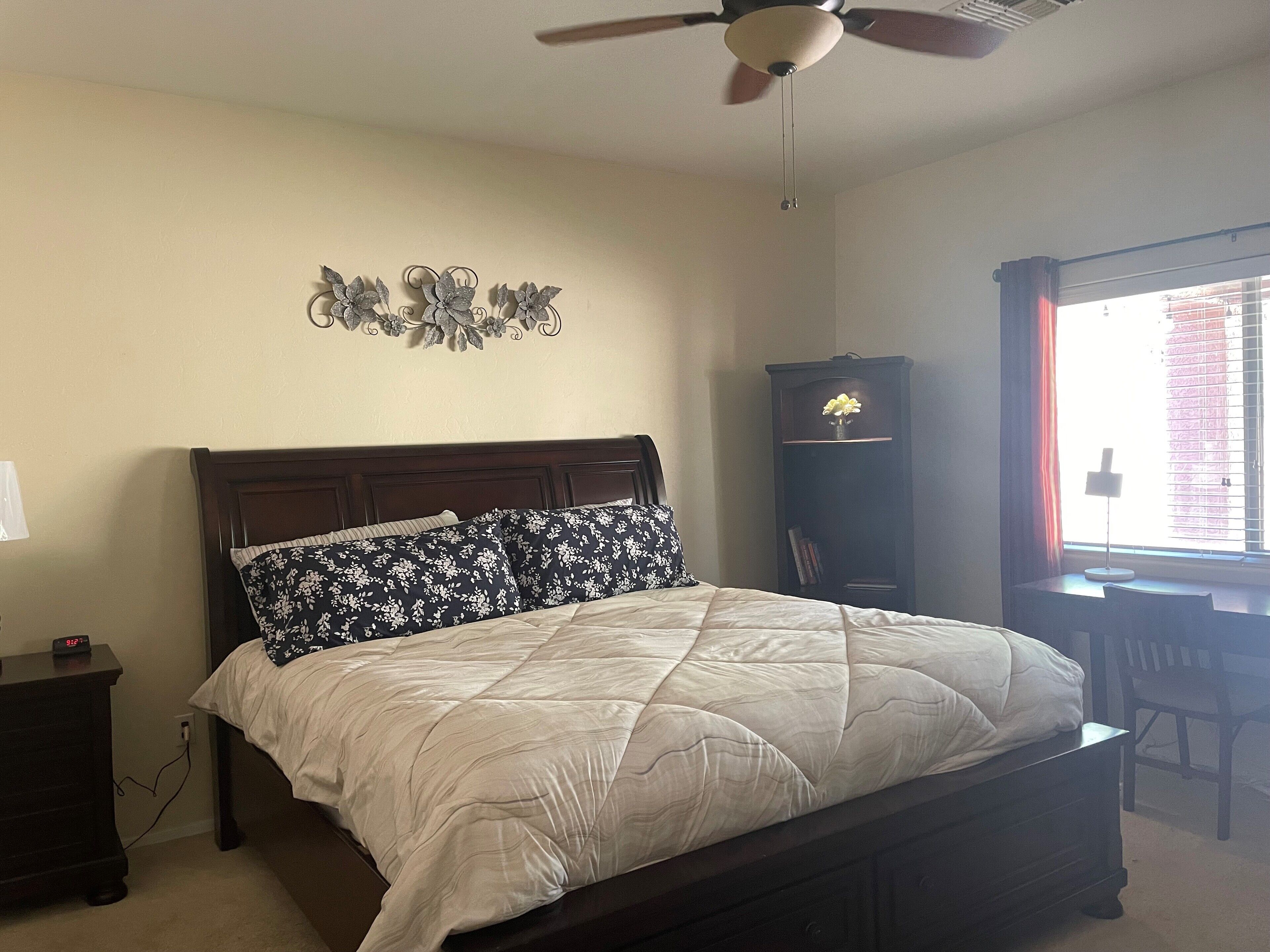 A bedroom with a bed, a nightstand, a dresser, a desk, and a window with blinds.