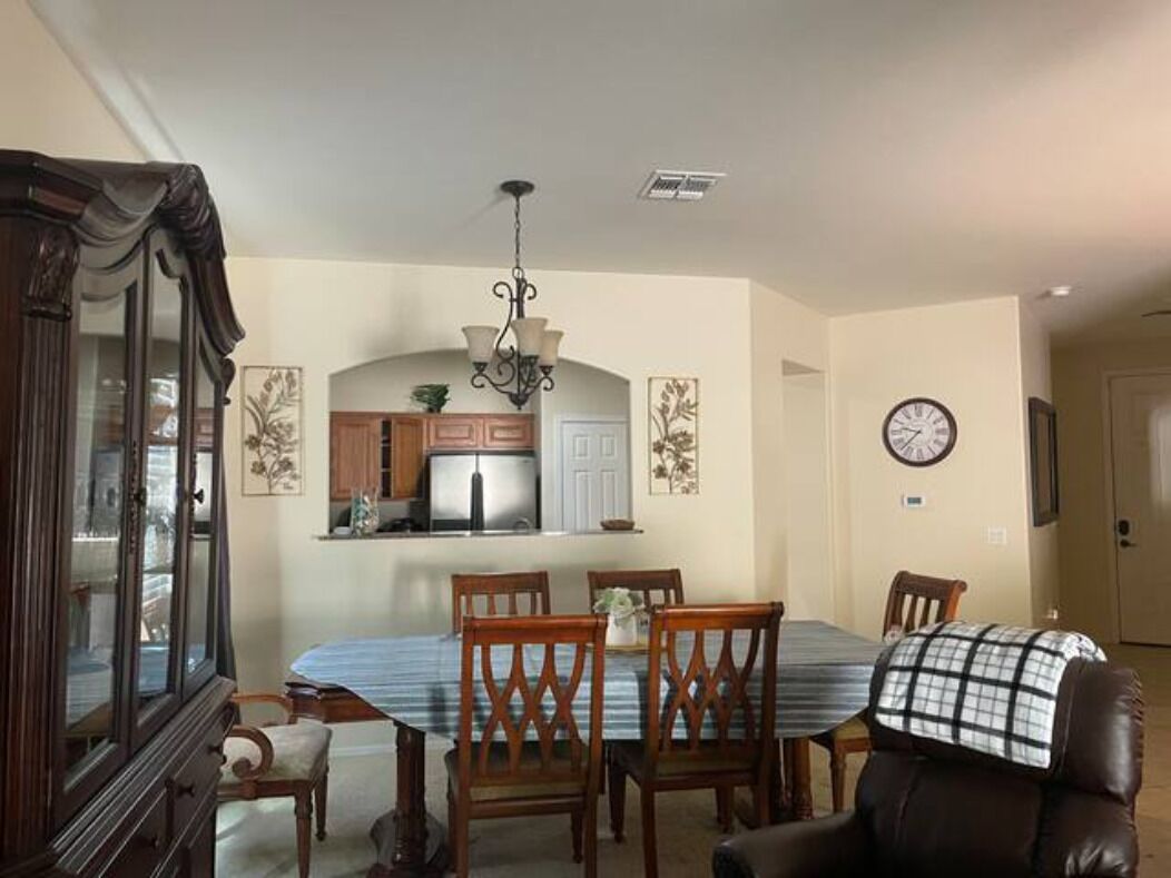 A dining area with a table, chairs, a chandelier, and a clock on the wall.