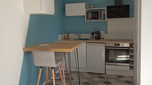 Une cuisine compacte avec une table et des chaises en bois, un four à micro-ondes, une cuisinière et un petit réfrigérateur.