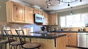 A kitchen with wooden cabinets, a central island with stools, a microwave, and a dishwasher. - Peaceful Forest Retreat w/ Pool, Game Room, EV Charger. Pet friendly!  (Grass Valley)