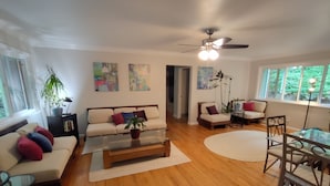 A modern living room with a sofa, coffee table, and chairs. There are paintings on the wall and a ceiling fan. - Peaceful Forest Retreat w/ Pool, Game Room, EV Charger. Pet friendly!  (Grass Valley)