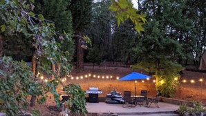 A backyard with a barbecue area, outdoor seating, a pool, and string lights. - Peaceful Forest Retreat w/ Pool, Game Room, EV Charger. Pet friendly!  (Grass Valley)