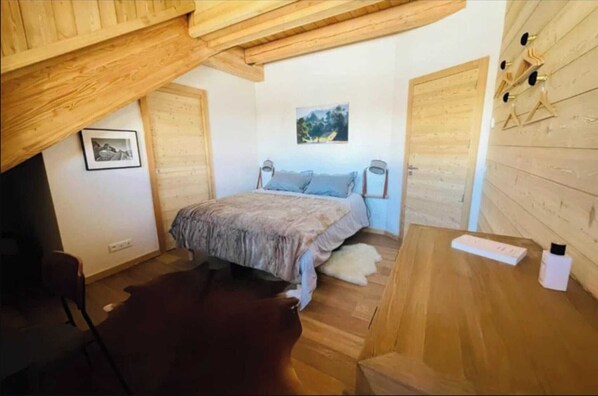 A bedroom with a bed, a wooden ceiling, a picture on the wall, and a small table with a bottle. - Chalet (Villard-Reculas)