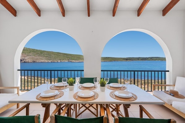 A dining table set for four with a view of the sea and hills.