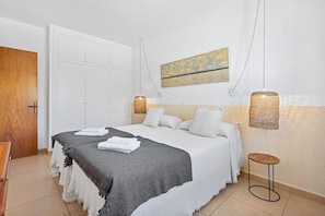A bedroom with a bed, white walls, a wooden door, a painting, and two wall-mounted lamps.