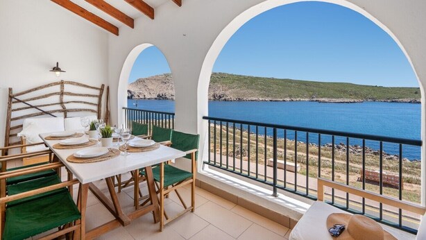 Un balcón con una mesa dispuesta para comer, con vistas al paisaje costero.