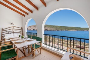 A balcony with a table set for dining, overlooking a coastal landscape.