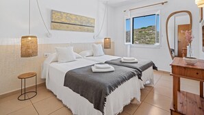 Habitación de hotel con dos camas, un ventanal con vistas, un aparador de madera y un espejo adosado a la pared.