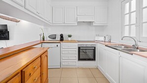 Una cocina compacta con muebles blancos, lavavajillas, horno, microondas, tostadora y pileta.