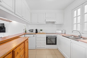A compact kitchen with white cabinetry, a dishwasher, an oven, a microwave, a toaster, and a sink.