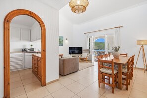 Een moderne keuken met witte kasten, een eethoek met een houten tafel en stoelen, een bank en een televisie.