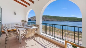 Un balcon avec une table dressée pour le dîner, offrant une vue sur une étendue d’eau et un paysage vallonné.