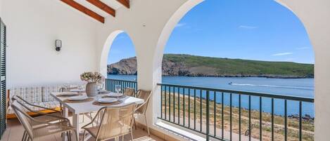 Un balcón con mesa lista para comer, con vista a una masa de agua y un paisaje montañoso.