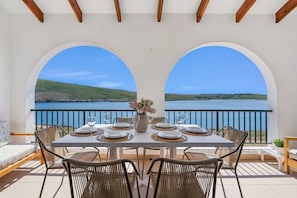 A dining table set for four with a view of a lake and hills. - Tramontana 115-P1 - Caressing the Mediterranean (Fornells)