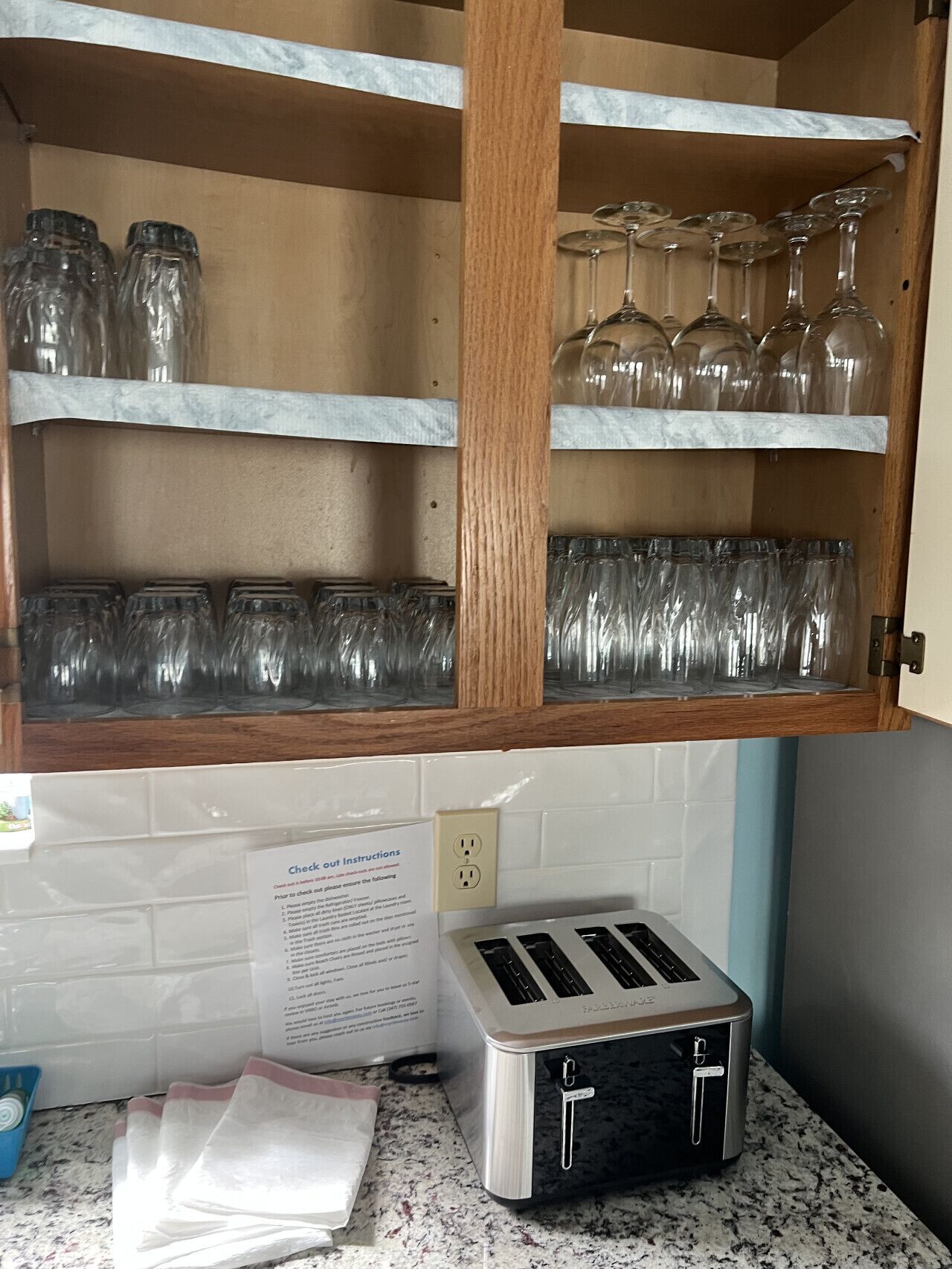 A kitchen with a wooden cabinet containing glass jars and wine glasses. There is a toaster on the counter.