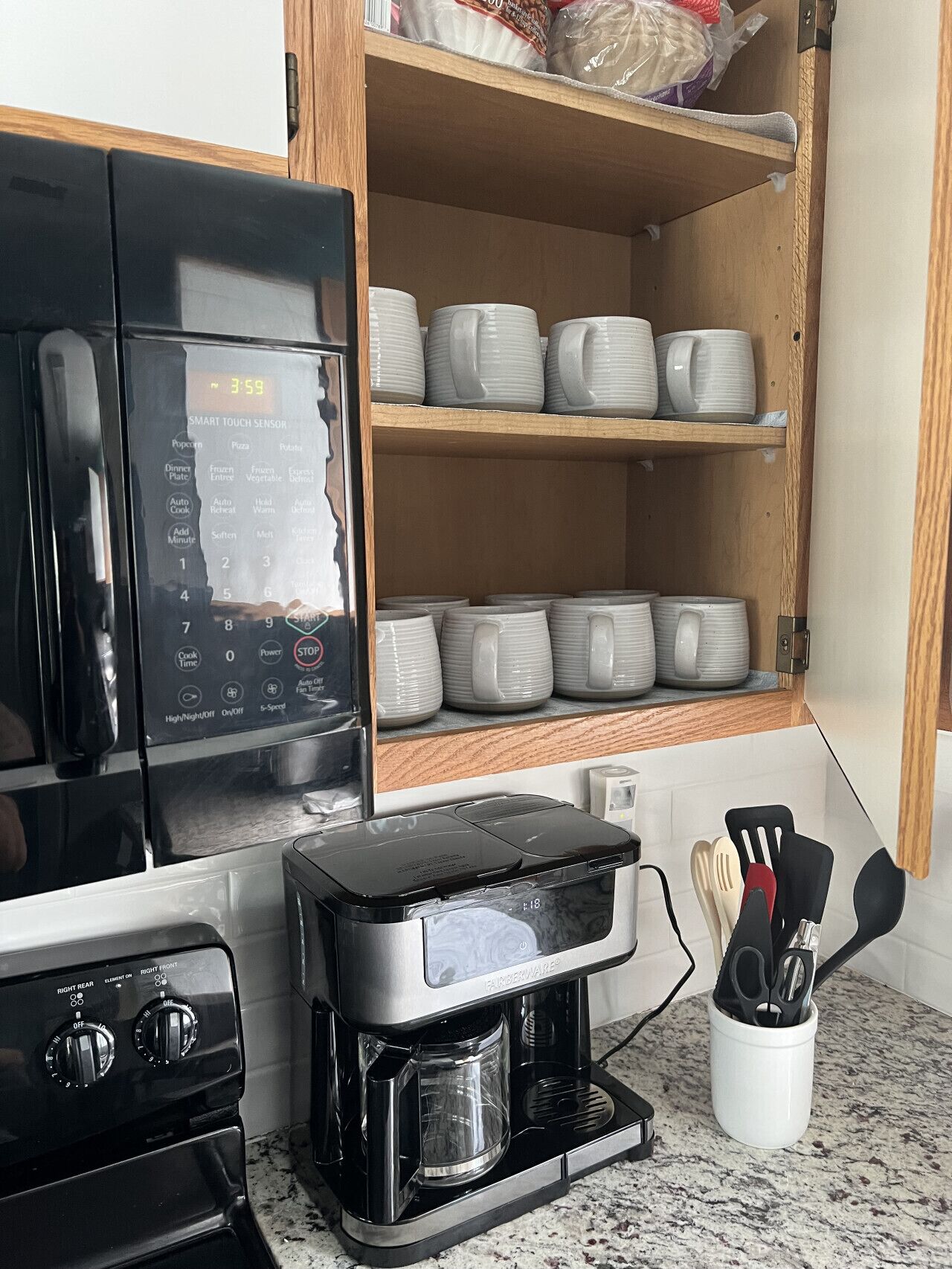 Une cuisine équipée d’un four à micro-ondes, d’une machine à café et d’un placard contenant des tasses blanches empilées.