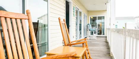 A wooden deck with chairs and tables, a white fence, and a building with large windows and doors.