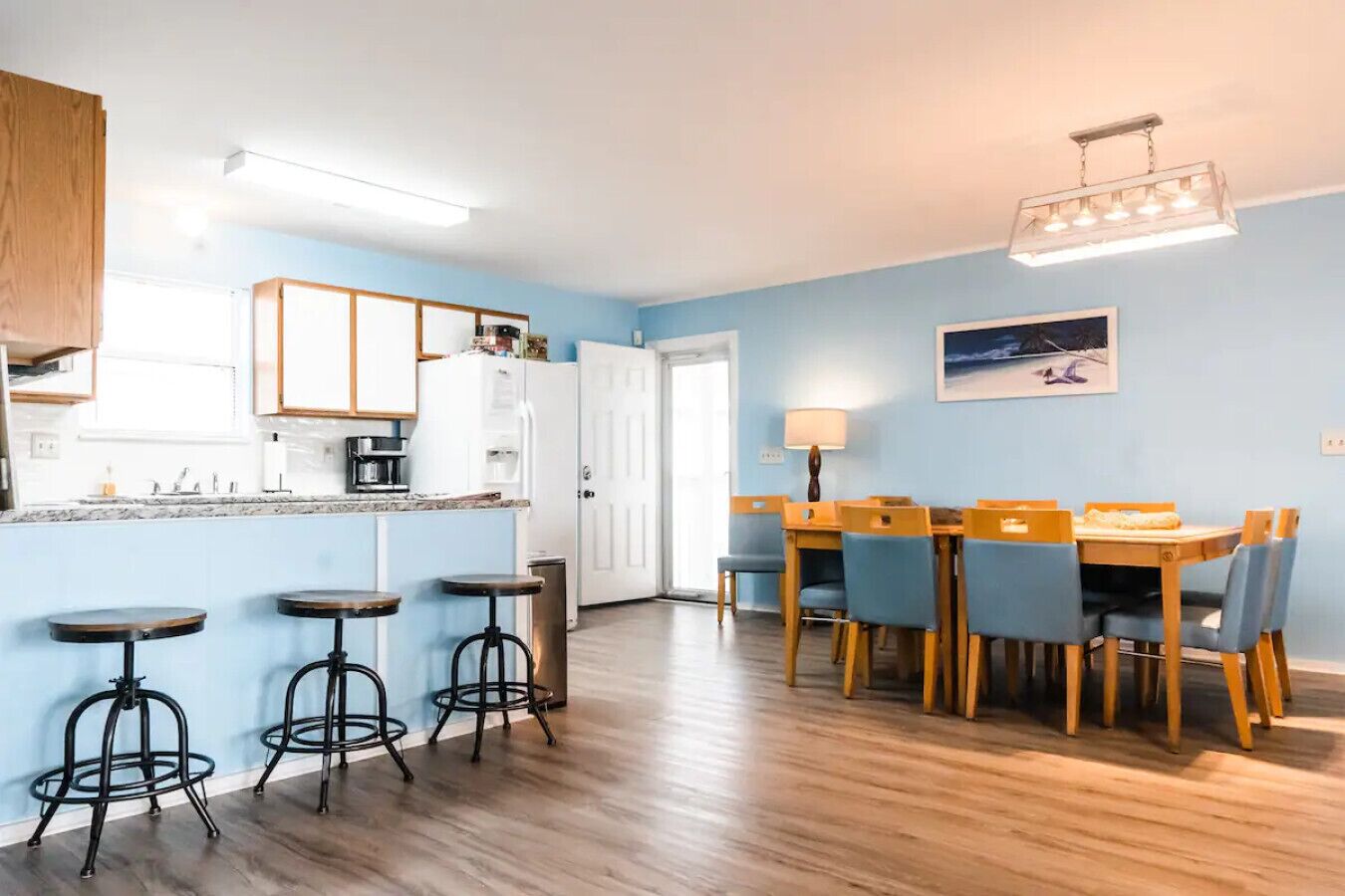 A modern kitchen with white cabinets, a dining area with wooden chairs and a table, and a bar stool area.