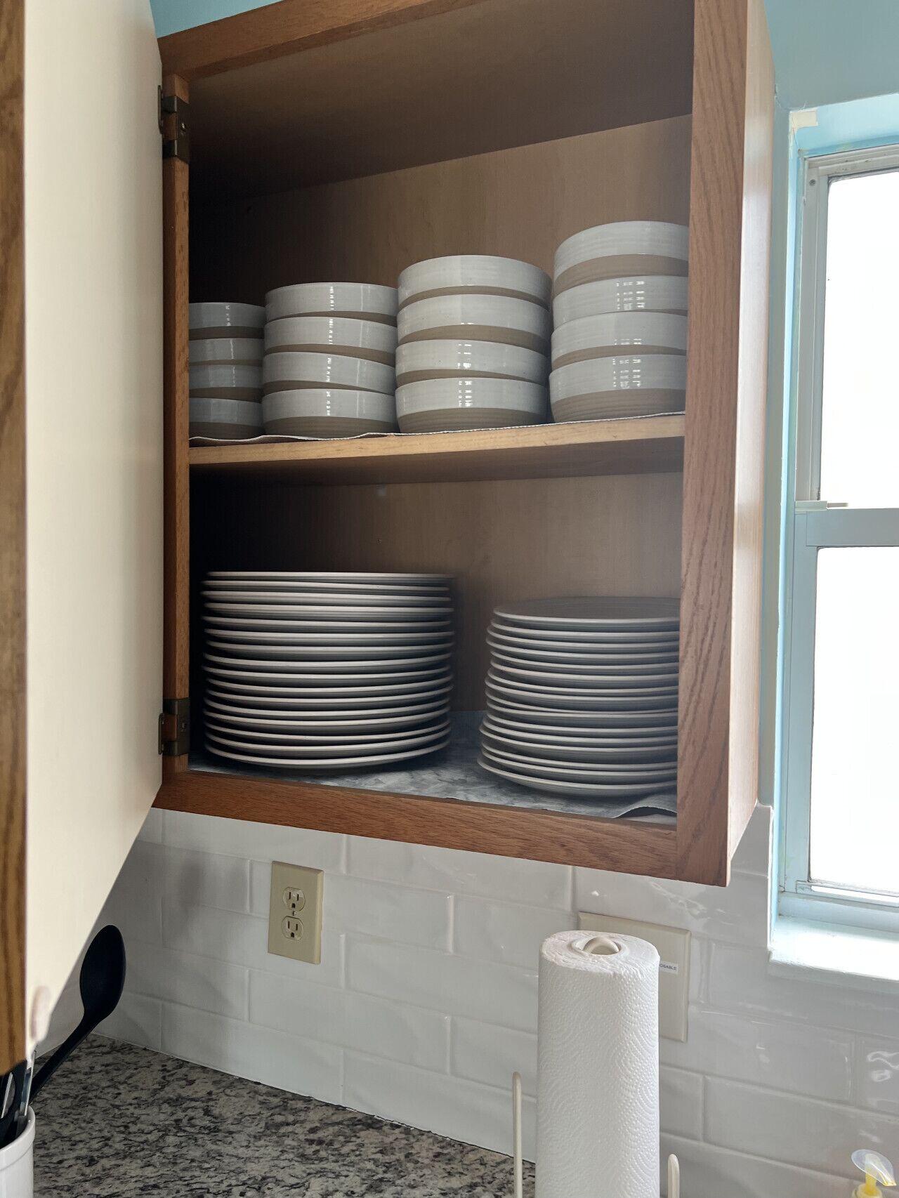 Una cocina con un armario de madera que contiene platos y tazones apilados.