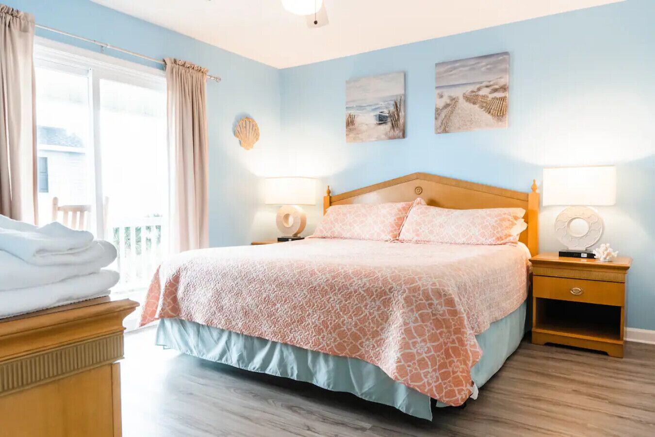 A bedroom with a bed, bedside tables, a nightstand, a window with curtains, and artwork on the wall.