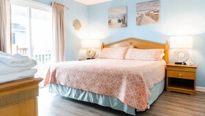 Un dormitorio con cama, mesitas de noche, una mesita auxiliar, una ventana con cortinas y una obra de arte en la pared.