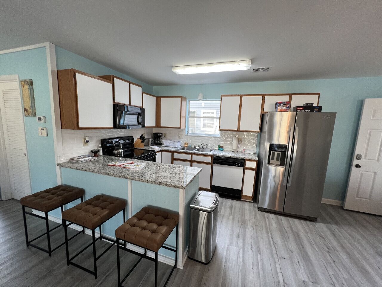 Una cocina moderna con una isla central, taburetes de bar, un refrigerador de acero inoxidable y un lavavajillas.