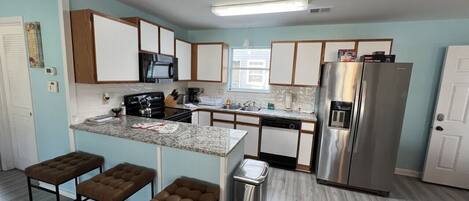 Una cocina moderna con una isla central, taburetes de bar, un refrigerador de acero inoxidable y un lavavajillas.
