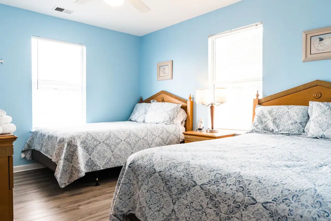 A room with two beds, each with a wooden headboard and a patterned bedspread. There are two bedside tables with lamps, and a framed picture on the wall.
