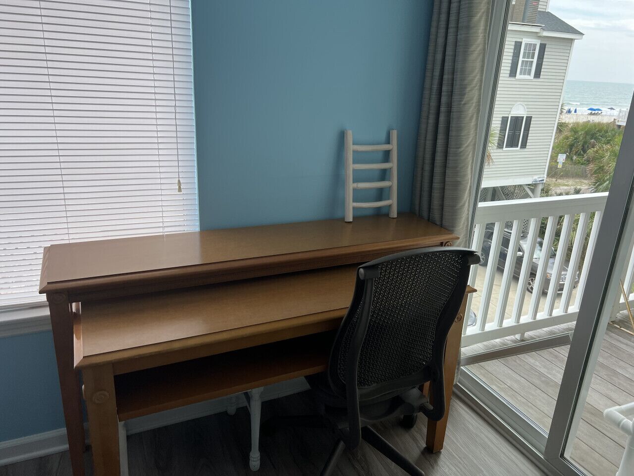 A wooden desk with a chair in a room with a blue wall and a view of the ocean.