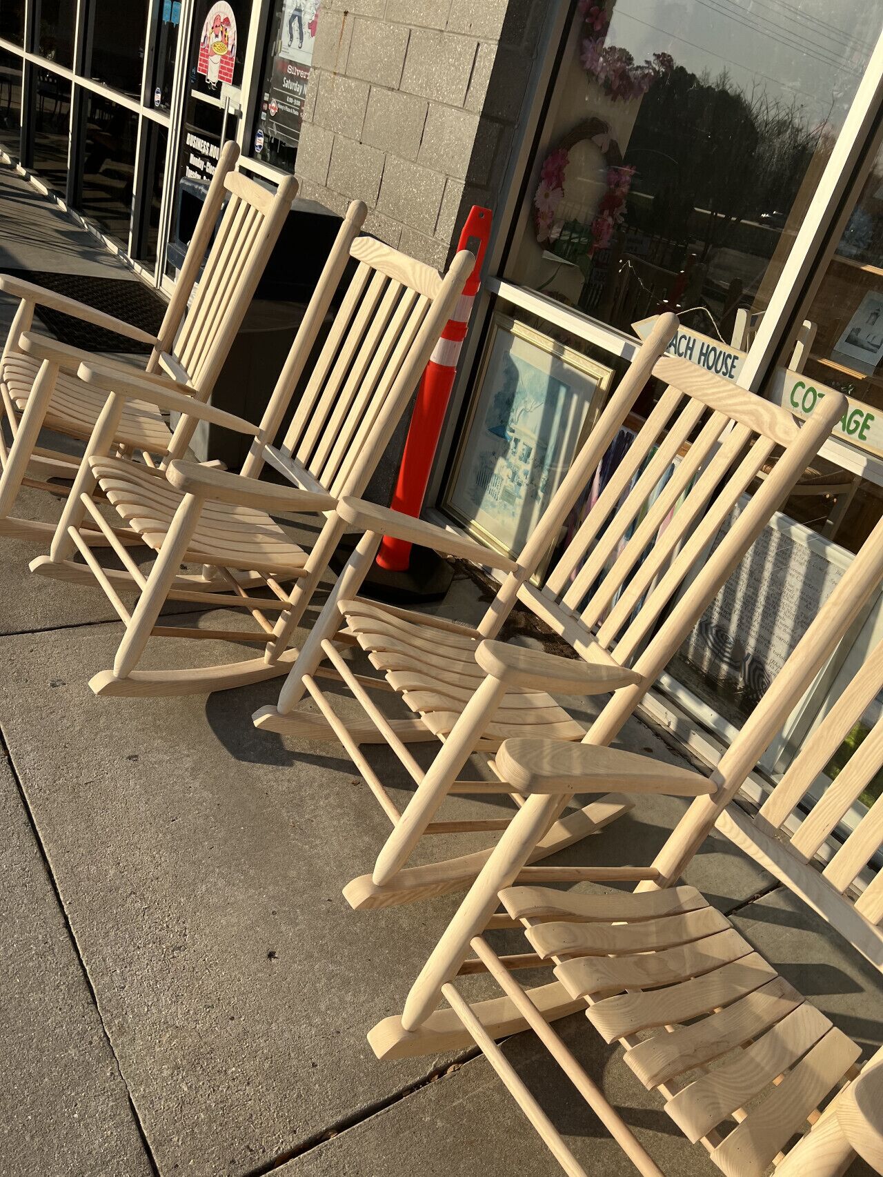 A row of wooden rocking chairs lined up outside a building with a sign that reads "Cottage House."
