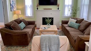 Un salon avec deux canapés marron, une petite table basse, une cheminée et un téléviseur fixé au-dessus.