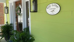 Un mur recouvert de végétation, sur lequel on peut lire l’inscription « Key Lime Cottage », et une porte ornée d’une guirlande.