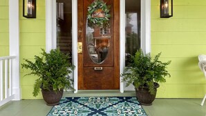 Une porte d’entrée ornée d’une guirlande décorative, deux plantes en pot et un tapis à motifs.