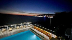 A pool area with lounge chairs and a view of the sea at night. - Planet Apartments (Sarandë)
