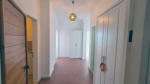 A hallway with a wooden door on the left, a white door in the center, and a white door on the right. There is a hanging light fixture above the center door.