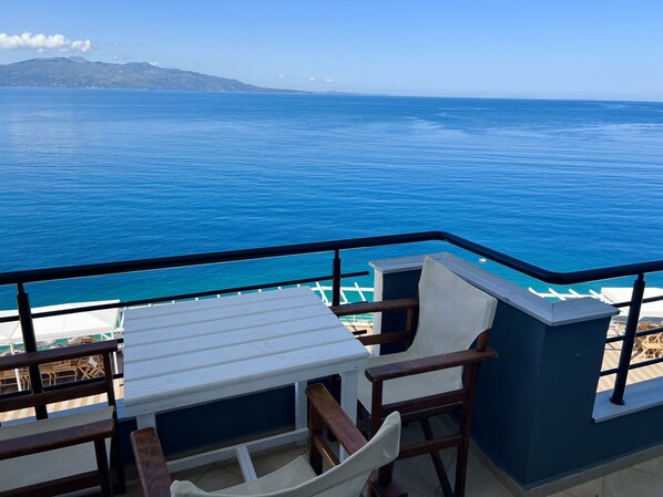 A balcony with a table and chairs overlooking a large body of water and distant mountains.